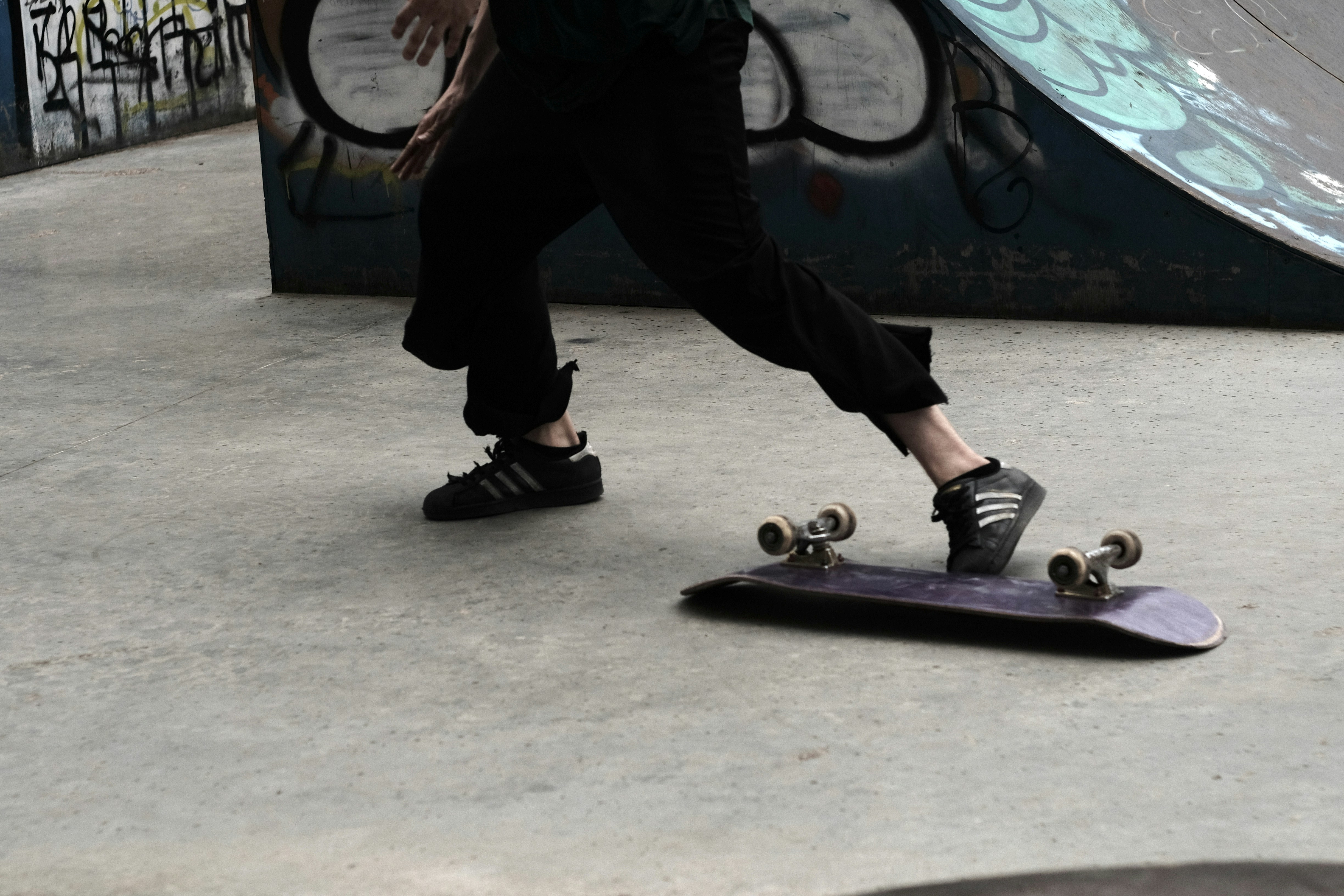 person in black pants and white sneakers standing on purple skateboard