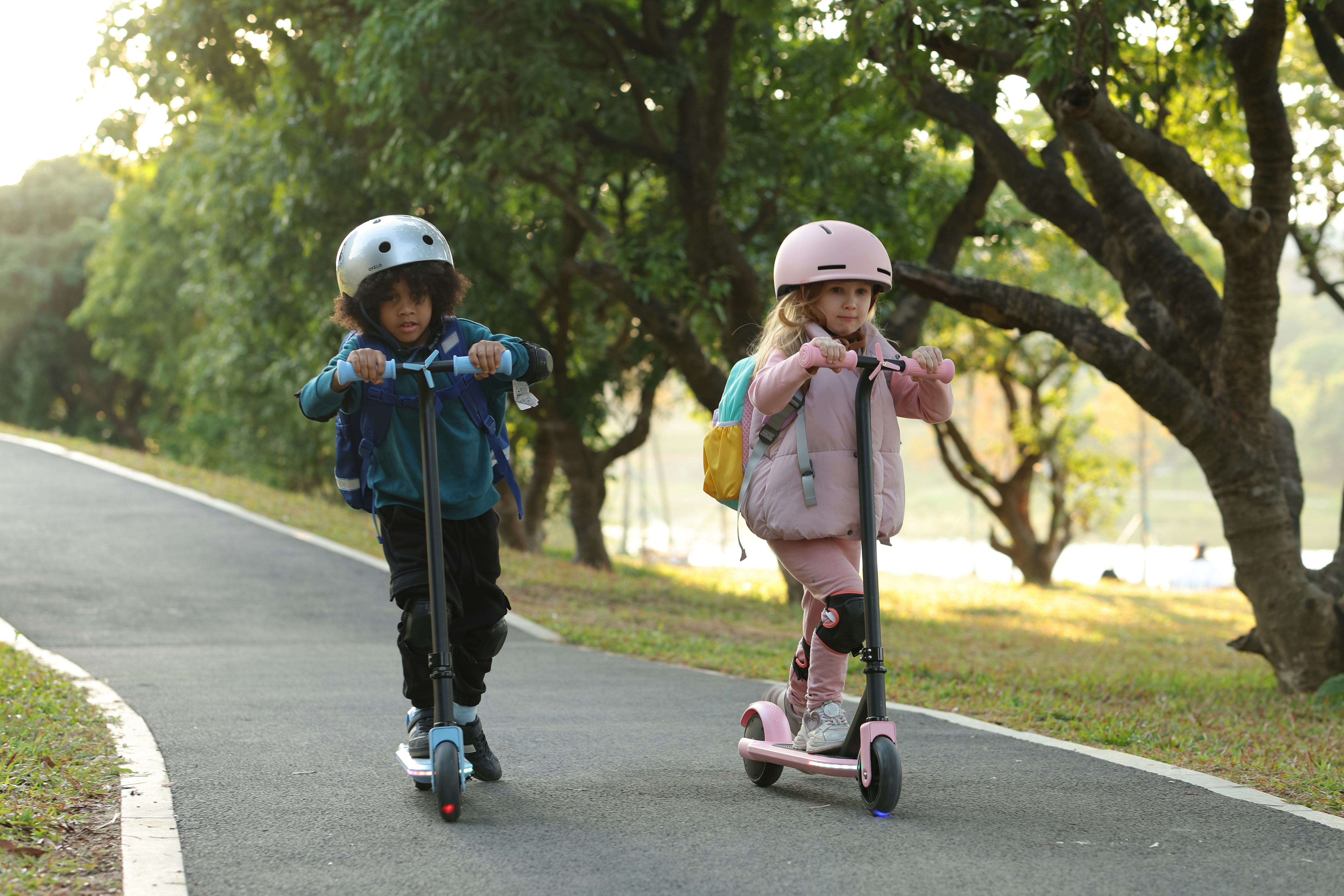 Two young children riding scooters down a road