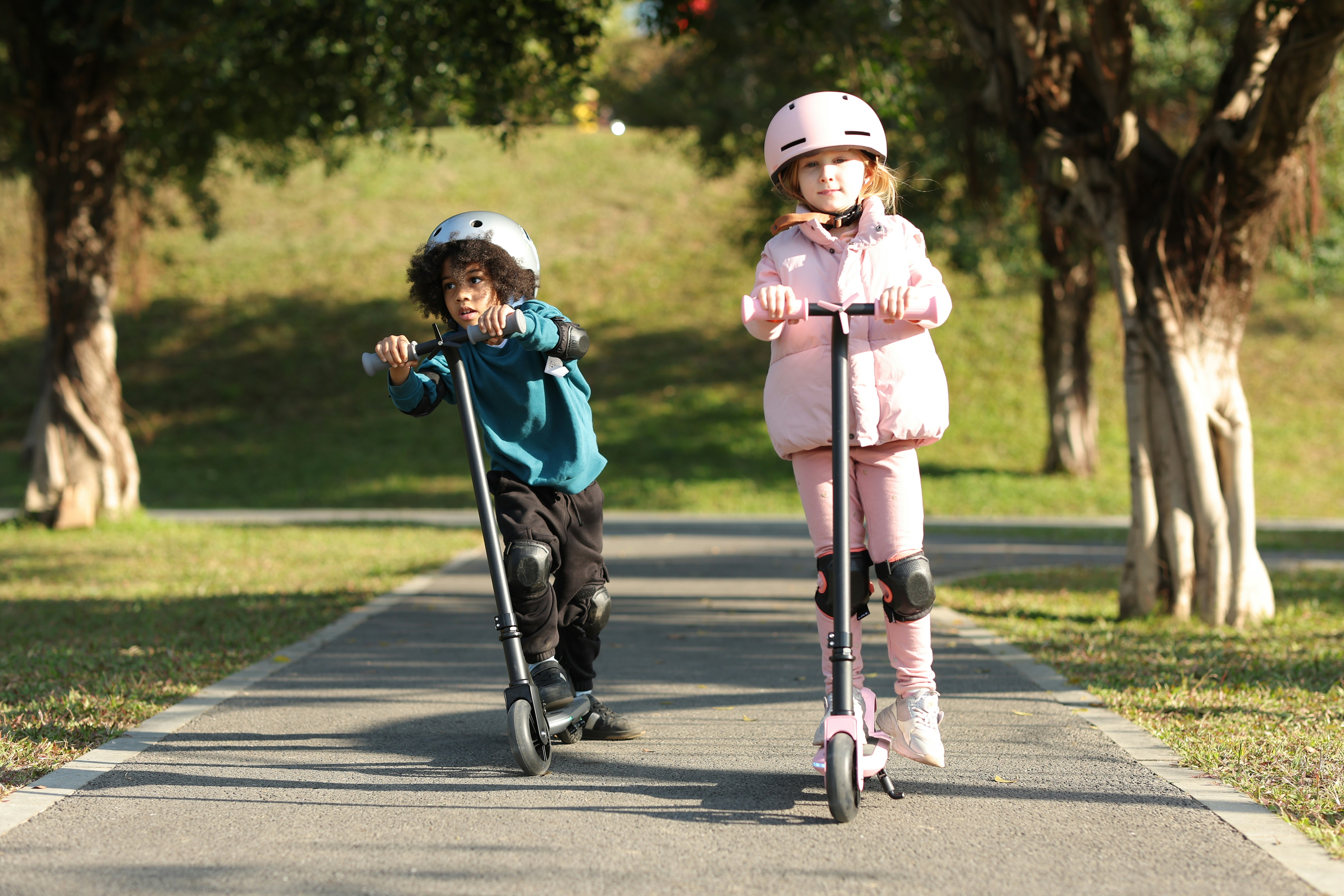 A couple of kids riding scooters down a road